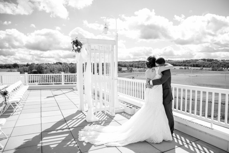 Black and white picture of a bride and groom embracing during their first look at a horse racing track,