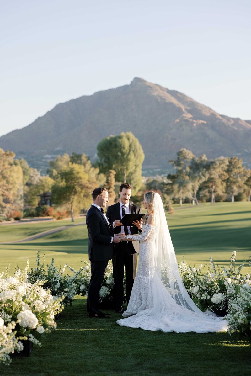 bride and groom surrounded by floral meadow during wedding ceremony in front of mountain view