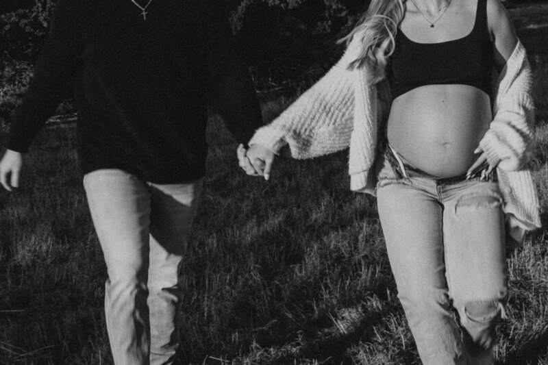 A pregnant woman is holding her partner's hand and walking in a field.