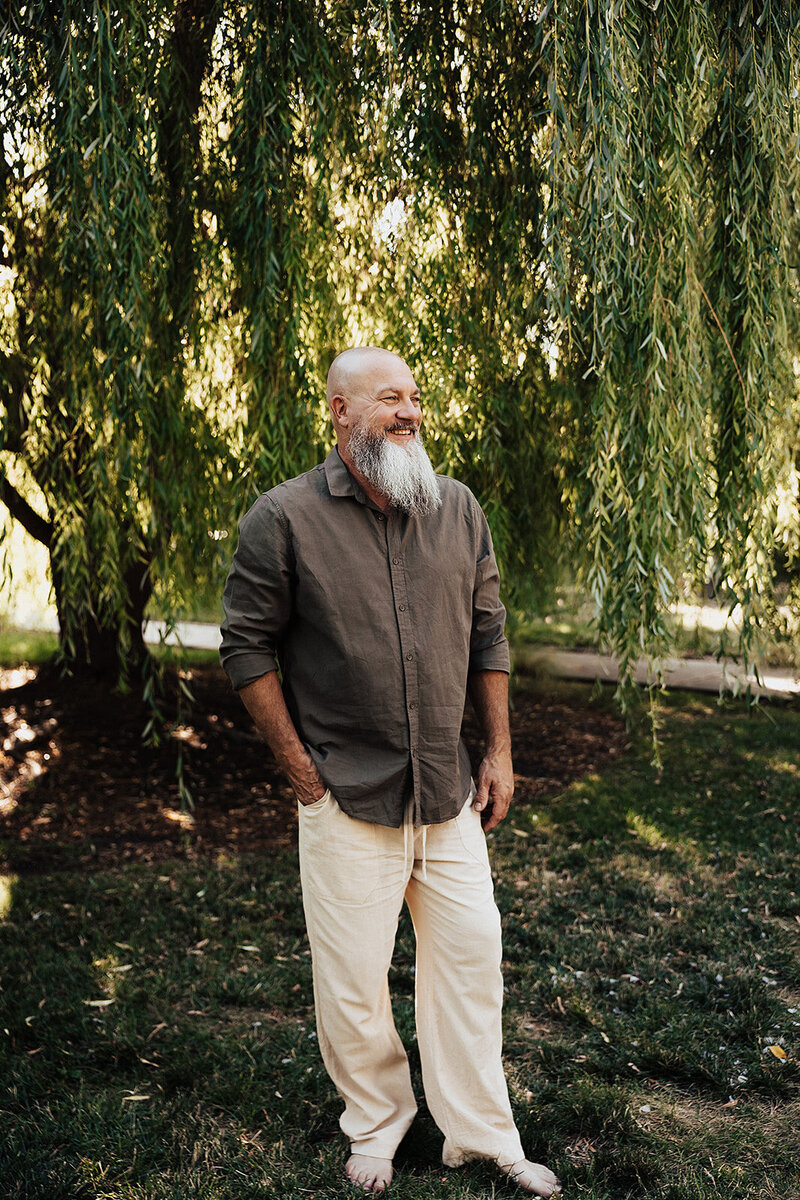 Jason standing in front of a tree smiling looking away from the camera 