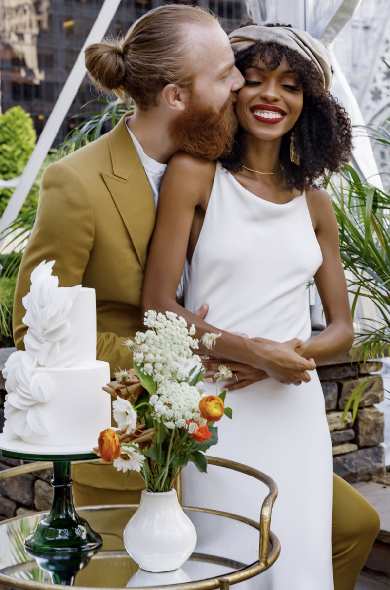 Bride and Groom embrace by their cake during a vow renewal ceremony with The We Do Collective at 620 Loft and Garden