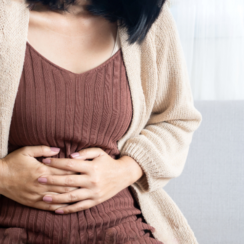 Woman holding her stomach with both hands, experiencing bloating or abdominal discomfort, symbolizing gut health and digestive issues.