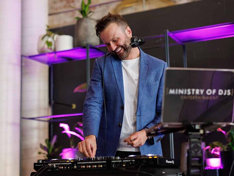 Male DJ smiling whilst mixing beats on their dJ decks