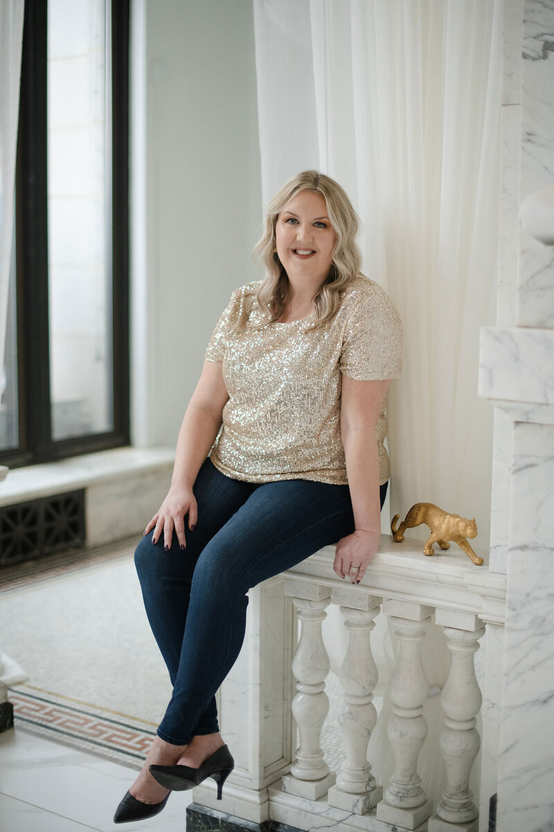 Melissa Lawrence smiles in a green dress while leaning on staircase railing