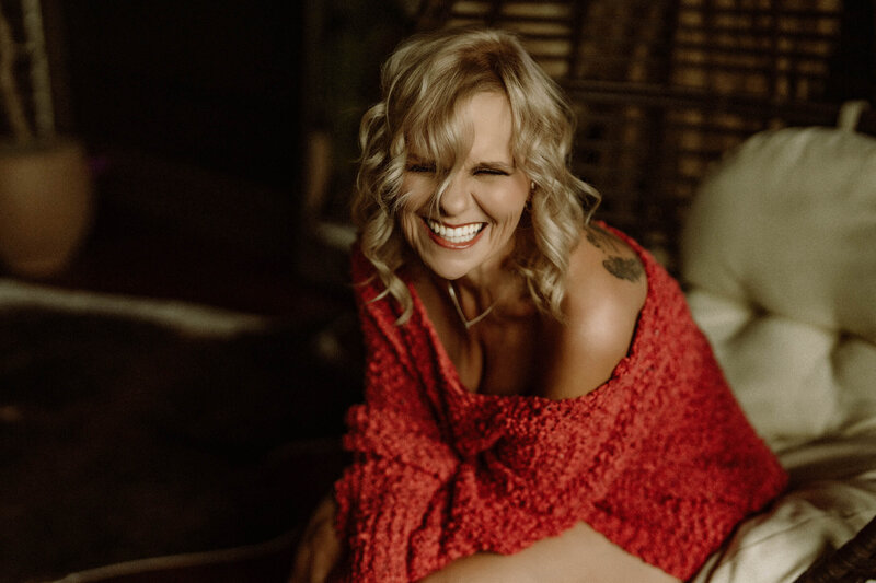 Woman laughing in cozy red sweater during boudoir session at Elevation Boudoir studio in Tuscaloosa, Alabama.