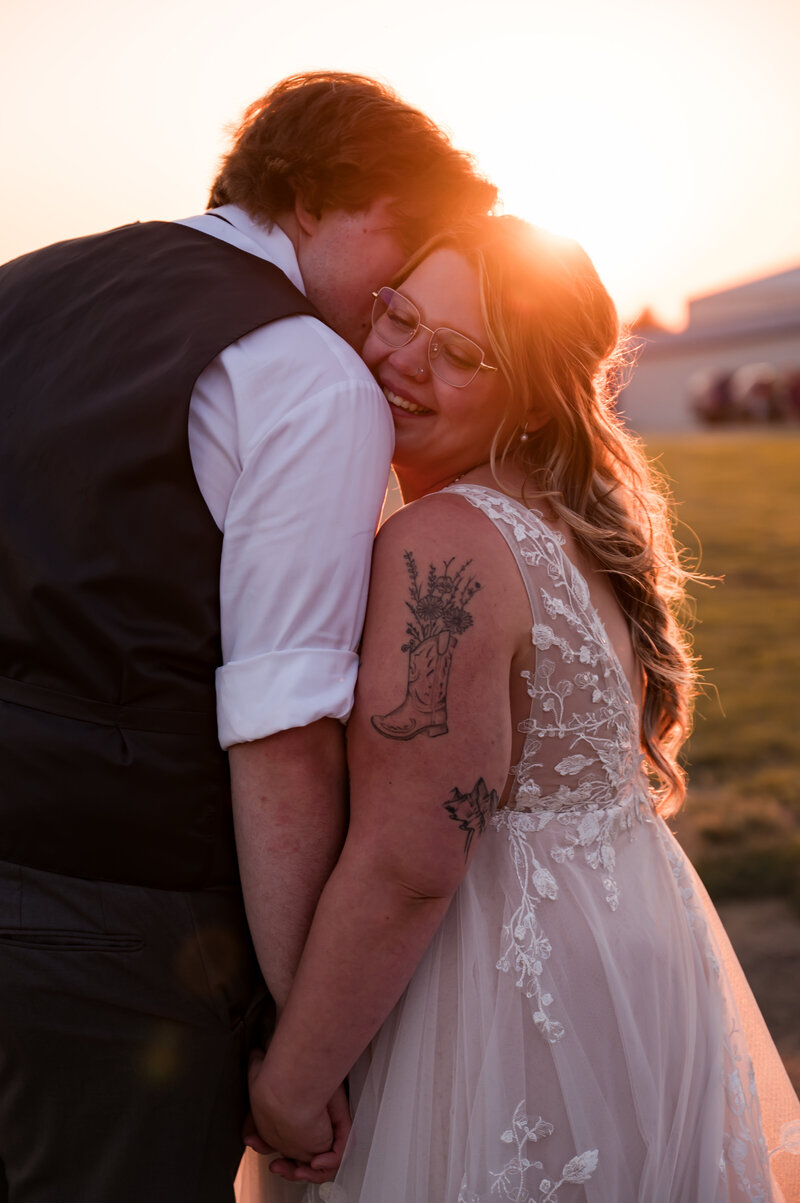 Groom gives bride a kiss on the cheek during sunset on their wedding day at Falkenberg Stables