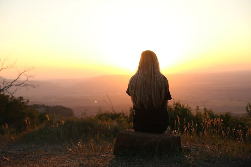 Blonde woman sitting on a rock looking at the sunset.