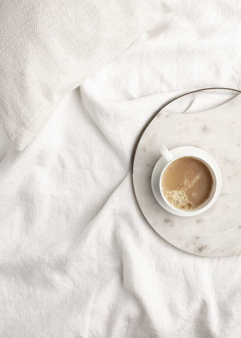 Mug of coffee on a clear plate sitting on top of white fabric