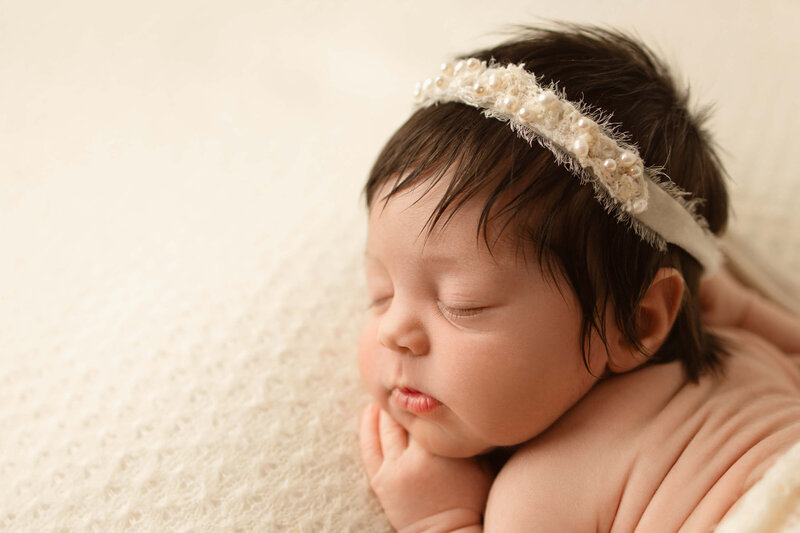 Newborn baby boy in a blue swaddle in a tan basket on a tan background