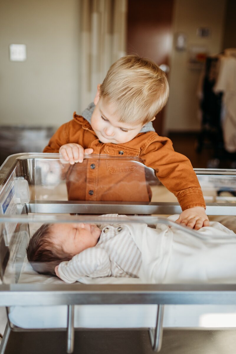 Big brother looking at baby brother in hospital bassinet