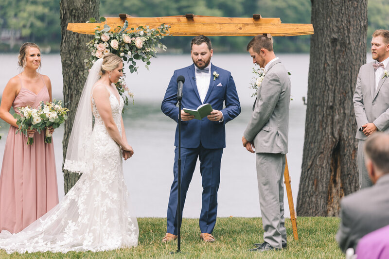 officiant in blue reads the wedding script to bride and groom along a lake shore captured by Scranton Wwedding Photographer Eric Boylan