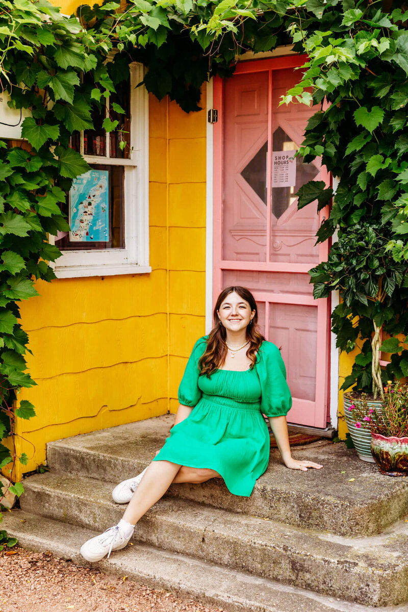 pretty brown haired teen in a kelly green dress sitting on the steps of a boutique in Fish Creek, Wisconsin
