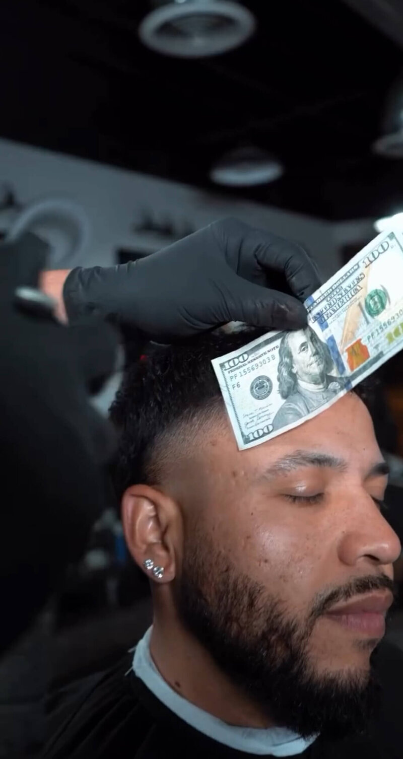 A barber uses a 100 dollar bill to line up a haircut at Onyx Barbershop in Wildomar, CA.
