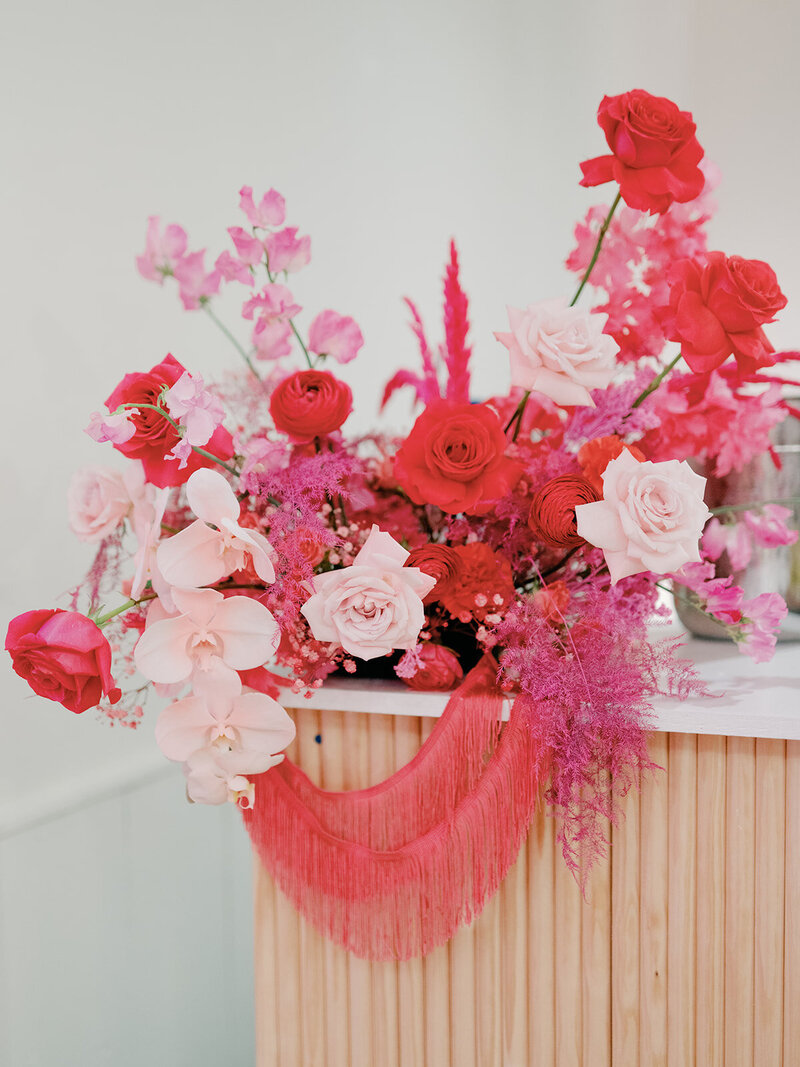 Bold pink and red floral arrangement with orchids and textural accents, designed for a dramatic corporate or wedding installation.