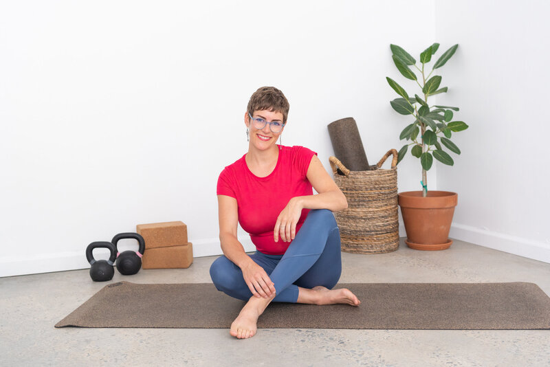 A woman sitting with yoga and workout equipment in the background.
