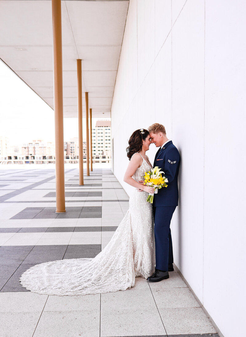 A wedding couple standing with their foreheads together leaning against a wall.