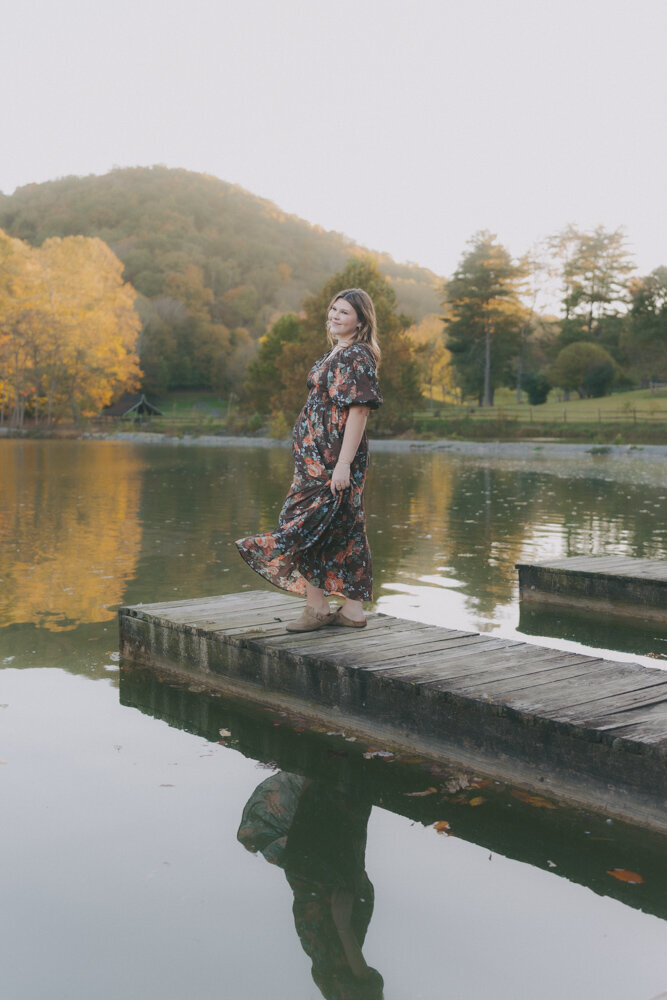 A young woman standing on a dock near the water at Steele Creek Park in Bristol, TN. She is looking out in the distance while playing with her dress. Northeast, TN Lifestyle Senior Photographer. 