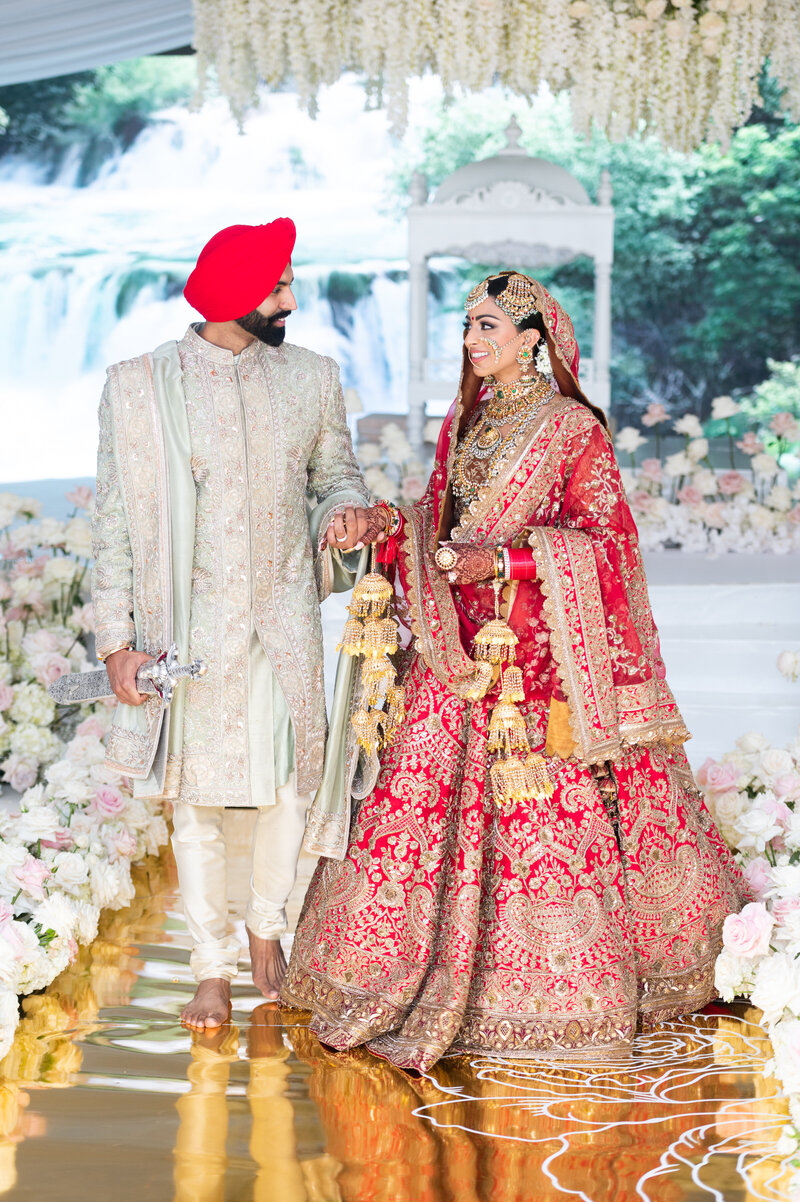 sikh couple holding hands in white and red attire while smiling