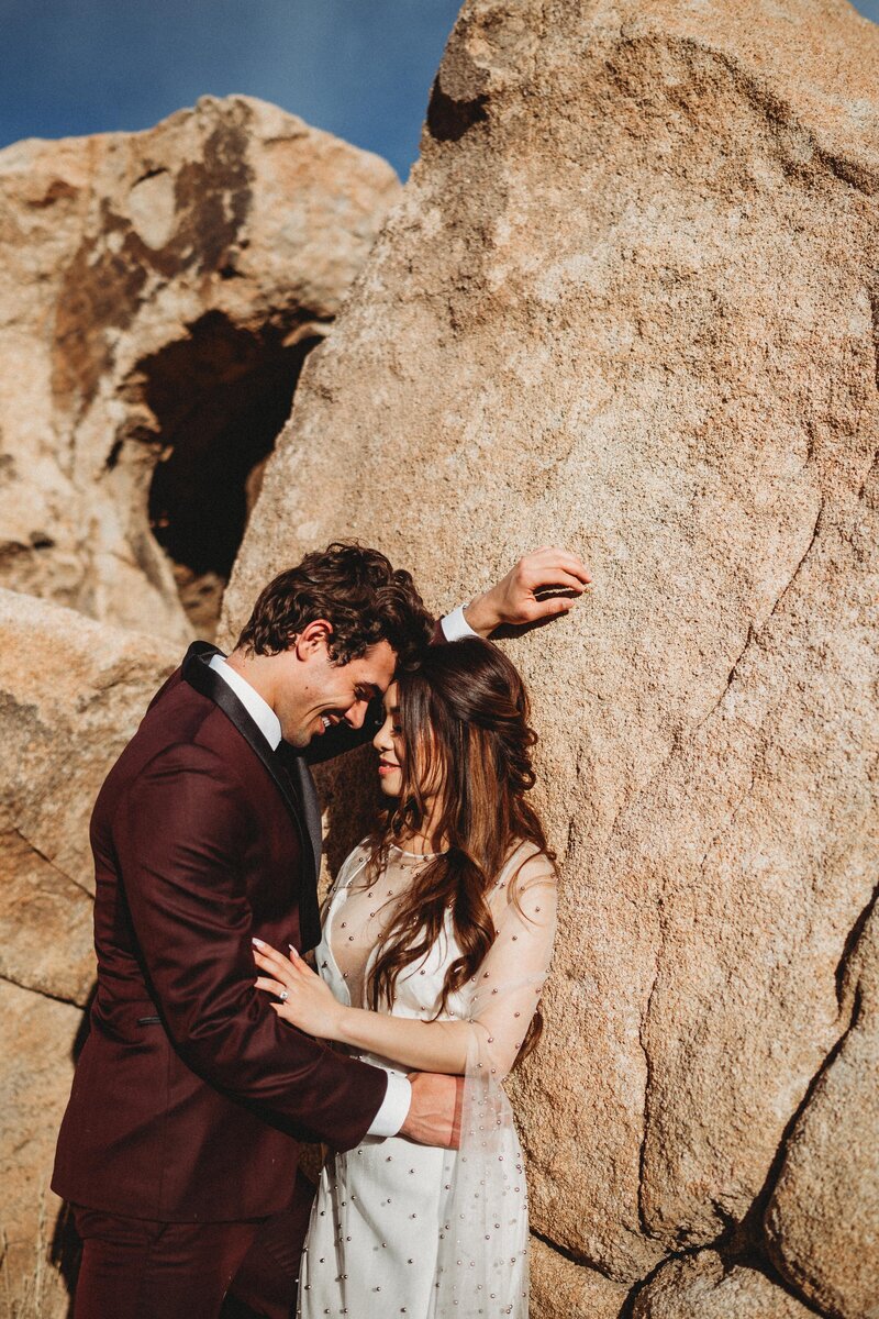 man wearing burgandy suit leaning into his bride elopement in the desert