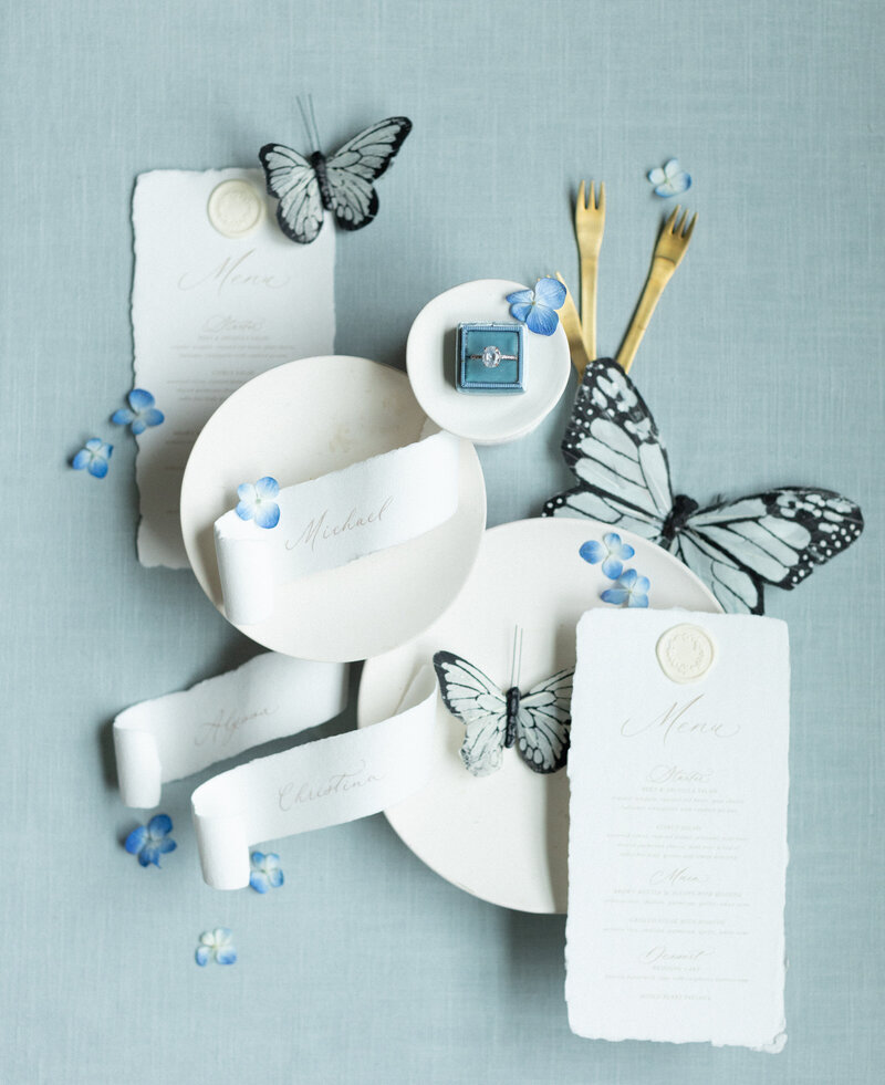 Soft blue linen flat lay mat styled with romantic paper goods and silk ribbon