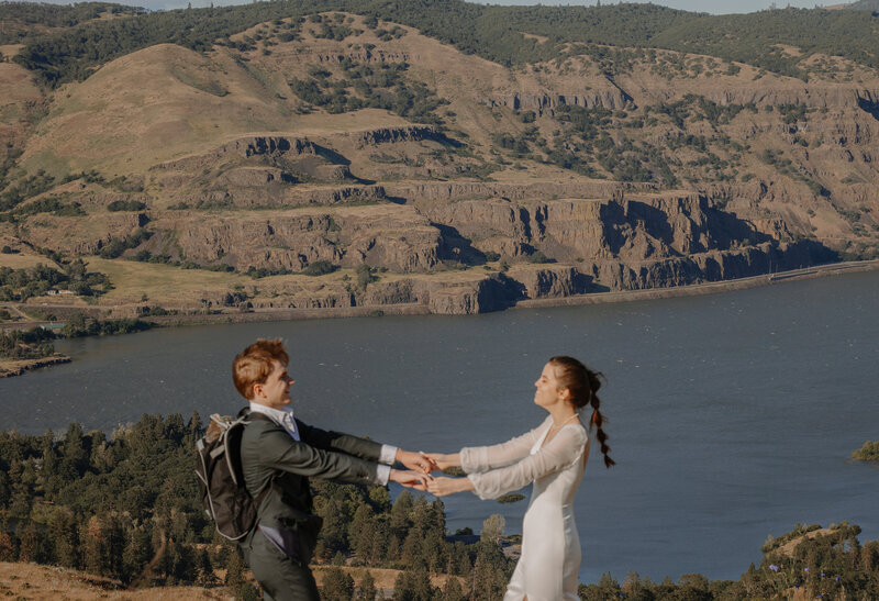 Bride and groom holding hands on a mountain overlooking a river