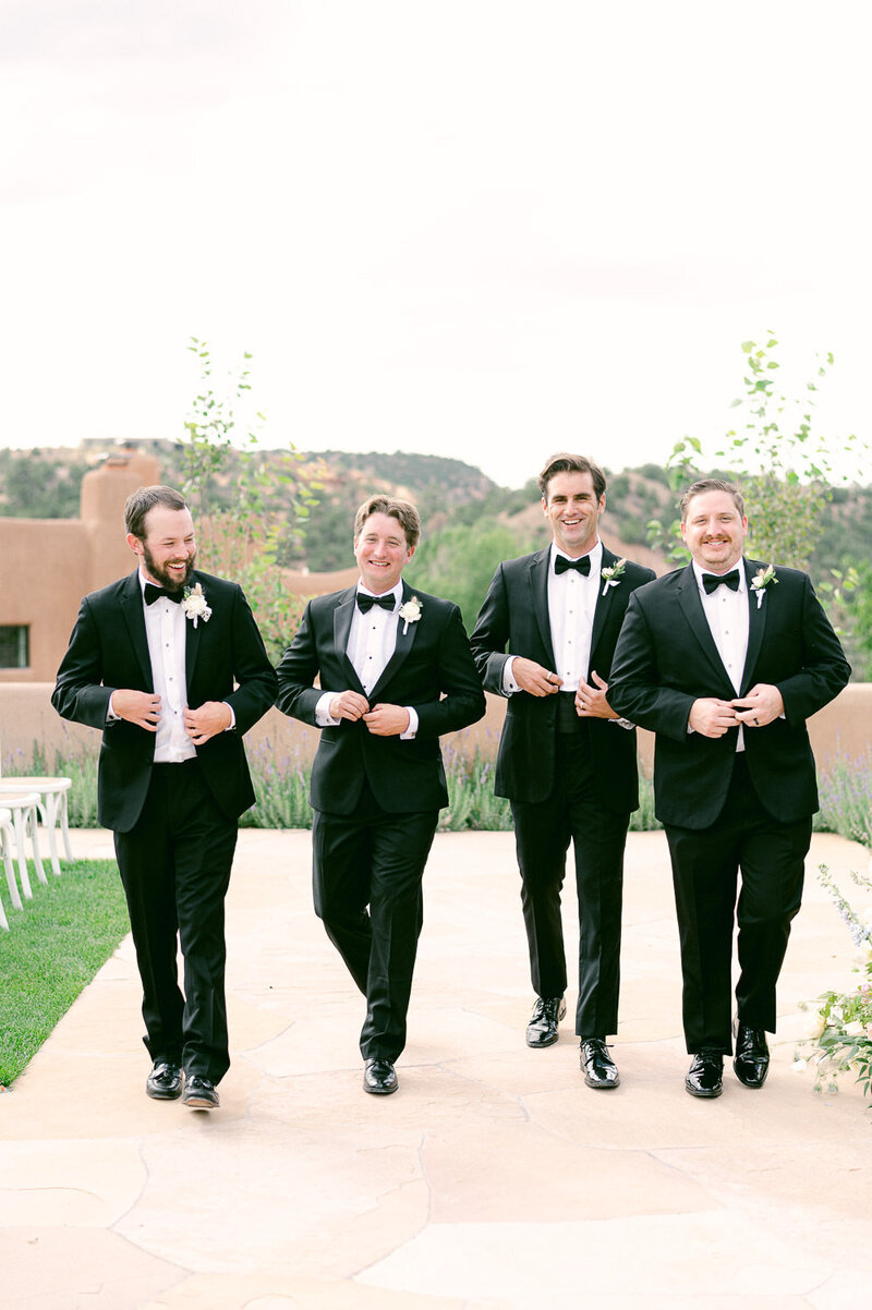 Groom and his grooms in tuxedos walk outside and smile