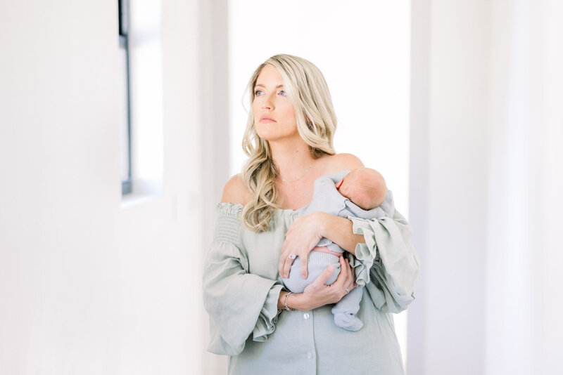 Blonde woman wearing a green dress and holding newborn baby for Tampa photographer Tina Marie Studio