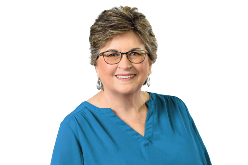 Carolyn Quintin, Midlife 50+ Career Coach, smiles in her headshot. She's wearing glasses, silver hoop earrings and a blue shirt