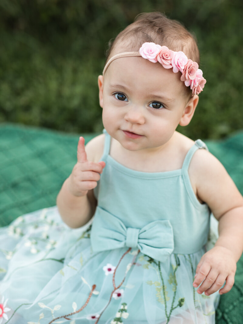 one year old girl sitting on green blanket for family photos