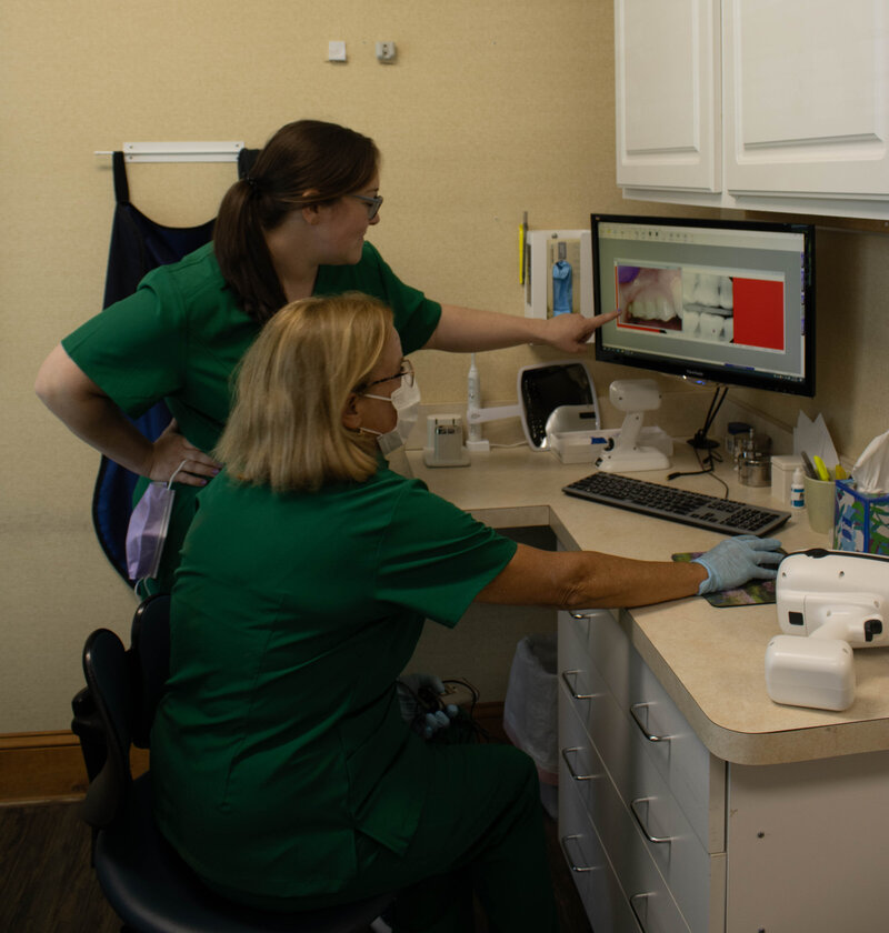 Two dental hygienists reviewing a patients chart at a computer.