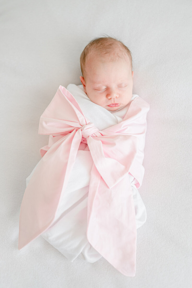 a newborn sleeps in a pink bow swaddle in Kristie Lloyd's full service photography sutdio