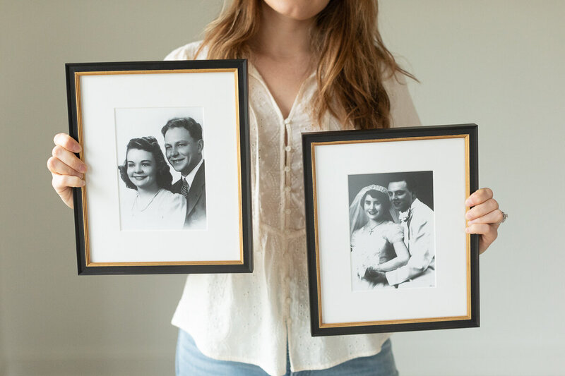 a woman holds antique photographs from family tree newly framed for a gallery wall