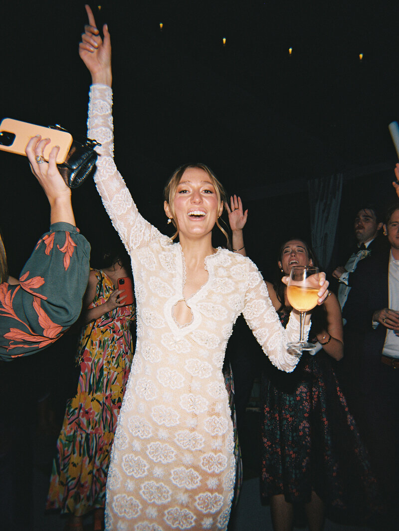 Flash film photo of bride holding wine glass and dancing surrounded by wedding guests