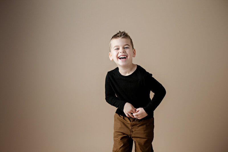 Toddler boy smiling standing in field of sunflowers.