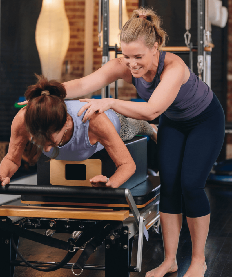 woman assisting a client holding a plan on a pilates reformer