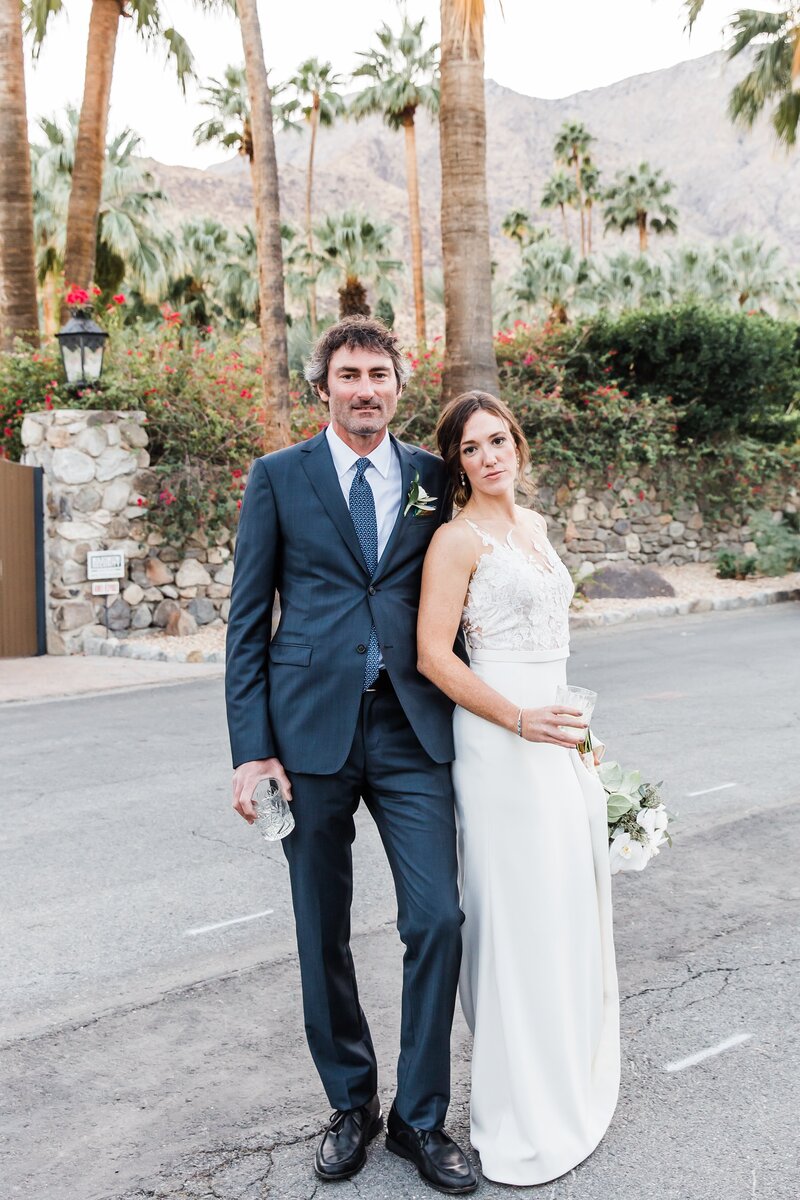 wedding couple posed and looking at the camera with a background of palm trees