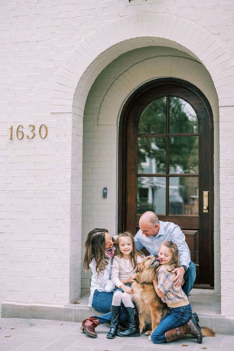 A family and their dog sitting in front of the front door of their house
