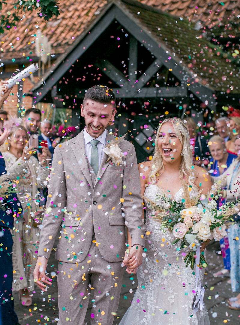 A very happy bride and groom walking hand in hand through a blizzard of confetti at their wedding