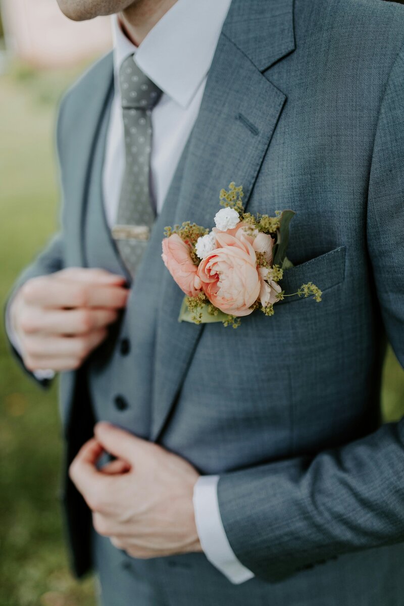 Groom in a stylish suit with a focus on the boutonniere, showcasing refined elegance and attention to detail for the wedding day ensemble.