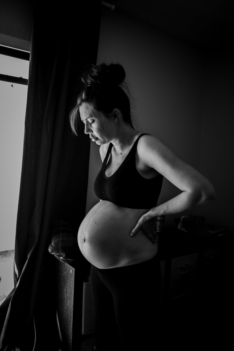 Black and white photo  of a pregnant woman standing in front of a window
