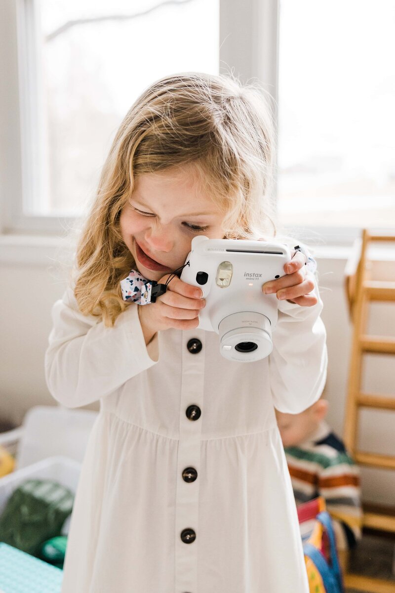 Young girl smiling while holding an instant camera up to her face, captured by a talented family photographer in Pittsburgh, PA.