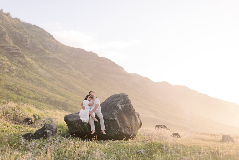 Couple sits together engaged on rock in Hawaii