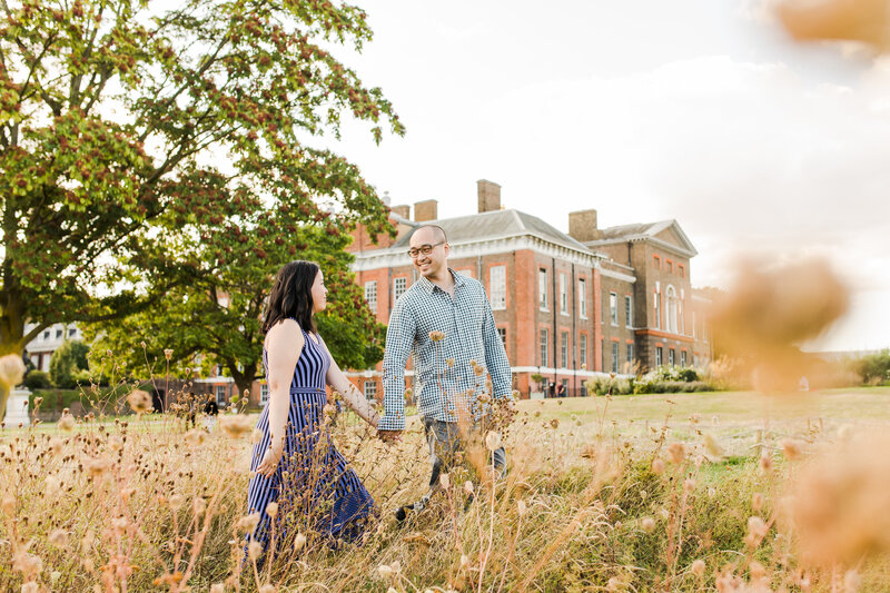 couple walking through long grass with kensington palace in the background