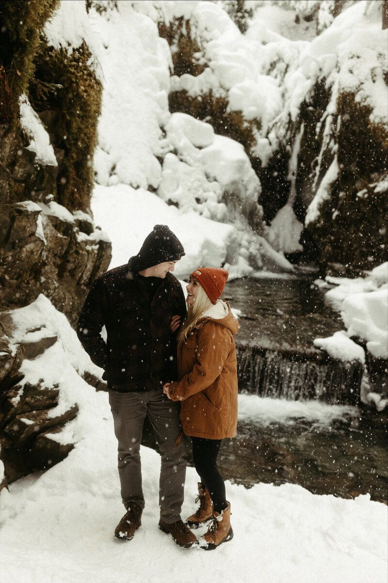 couple standing next to a waterfall during their snowy engagement session