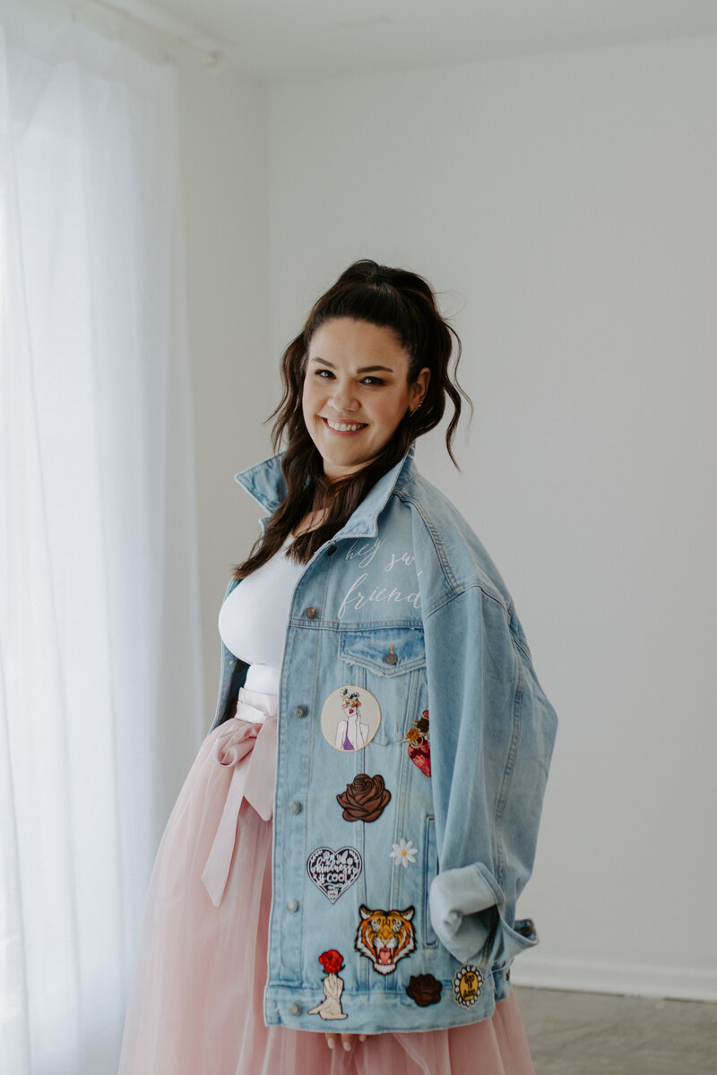 woman dark hair with arms up celebrating in jean jacket and pink skirt