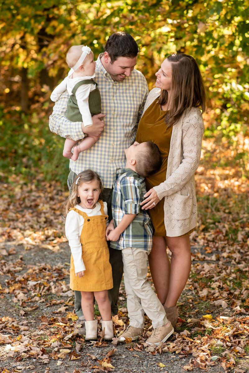 A candid picture of a family smiling at each other with fall leaves in the background