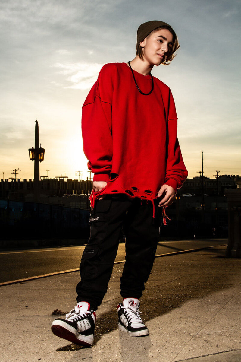 Dominique Ilie pre teen personal branding portrait full length shot wearing red sweatshirt black pants runners standing on street sunset in behind