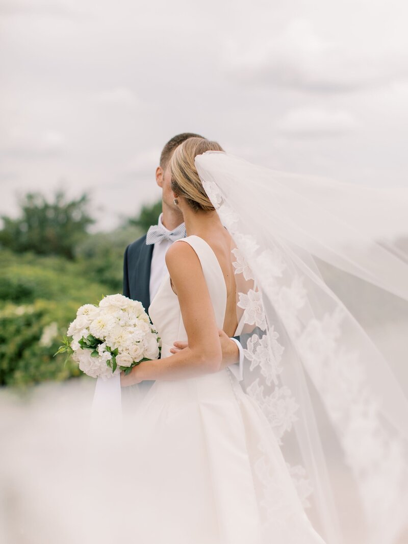 Bride and groom kissing with veil blowing toward camera