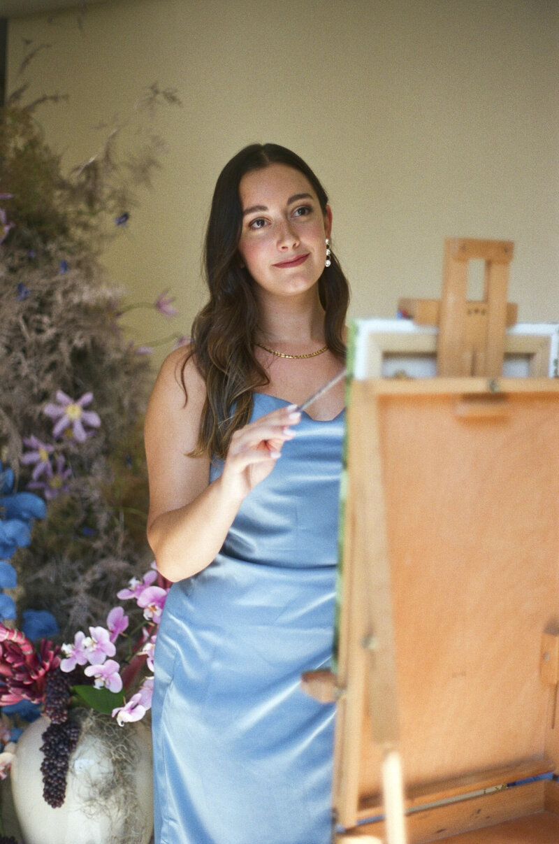 Sloan in a blue dress near a canvas