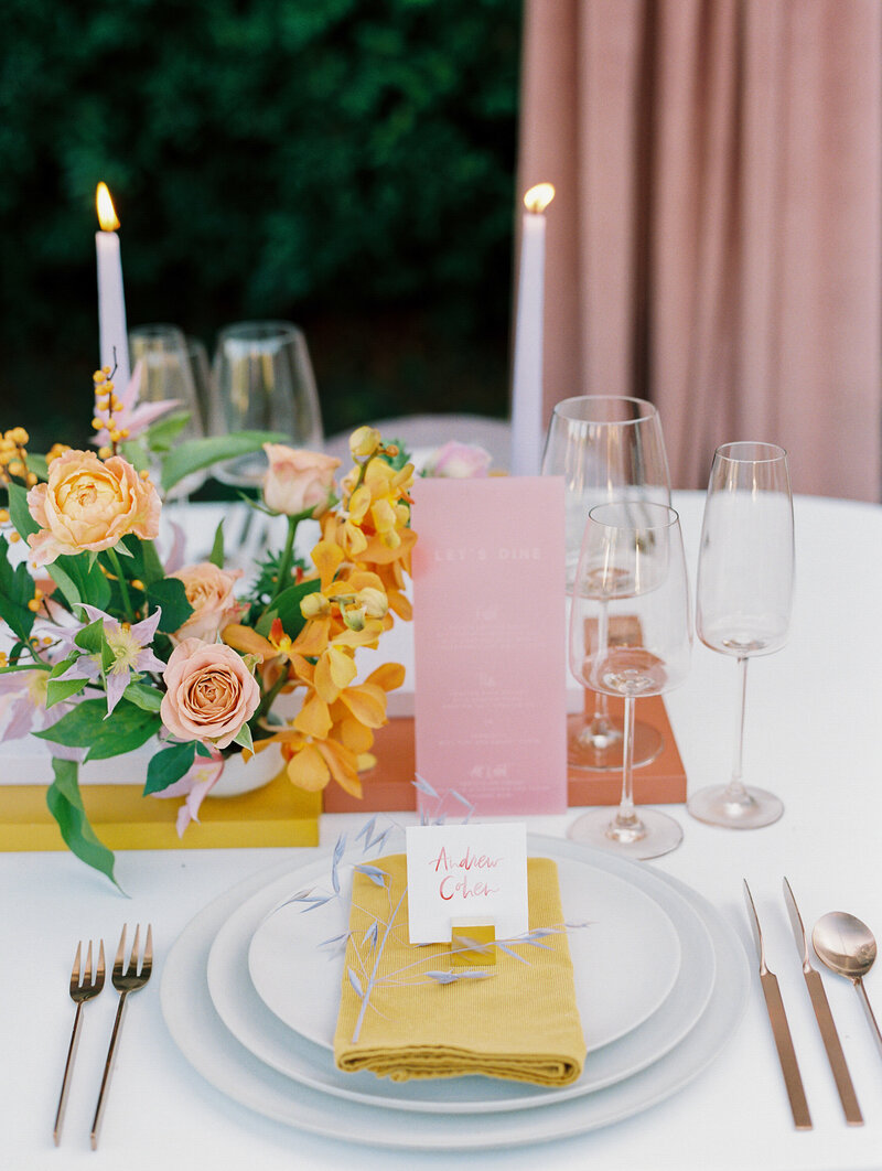 close up of place setting with three white plates, yellow courderoy napkin, and hand painted name card in pink with pink and purple florals surrounding